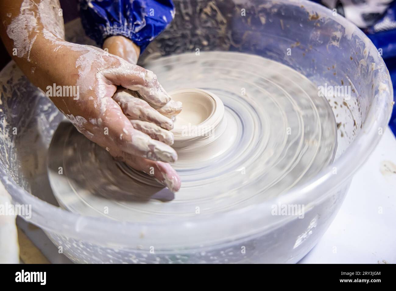 Hands of a clay sculpting teacher while teaching a child on a potter's wheel Stock Photo