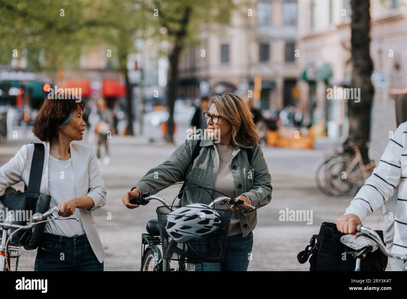 Senior female friends talking to each other while wheeling bicycles Stock Photo