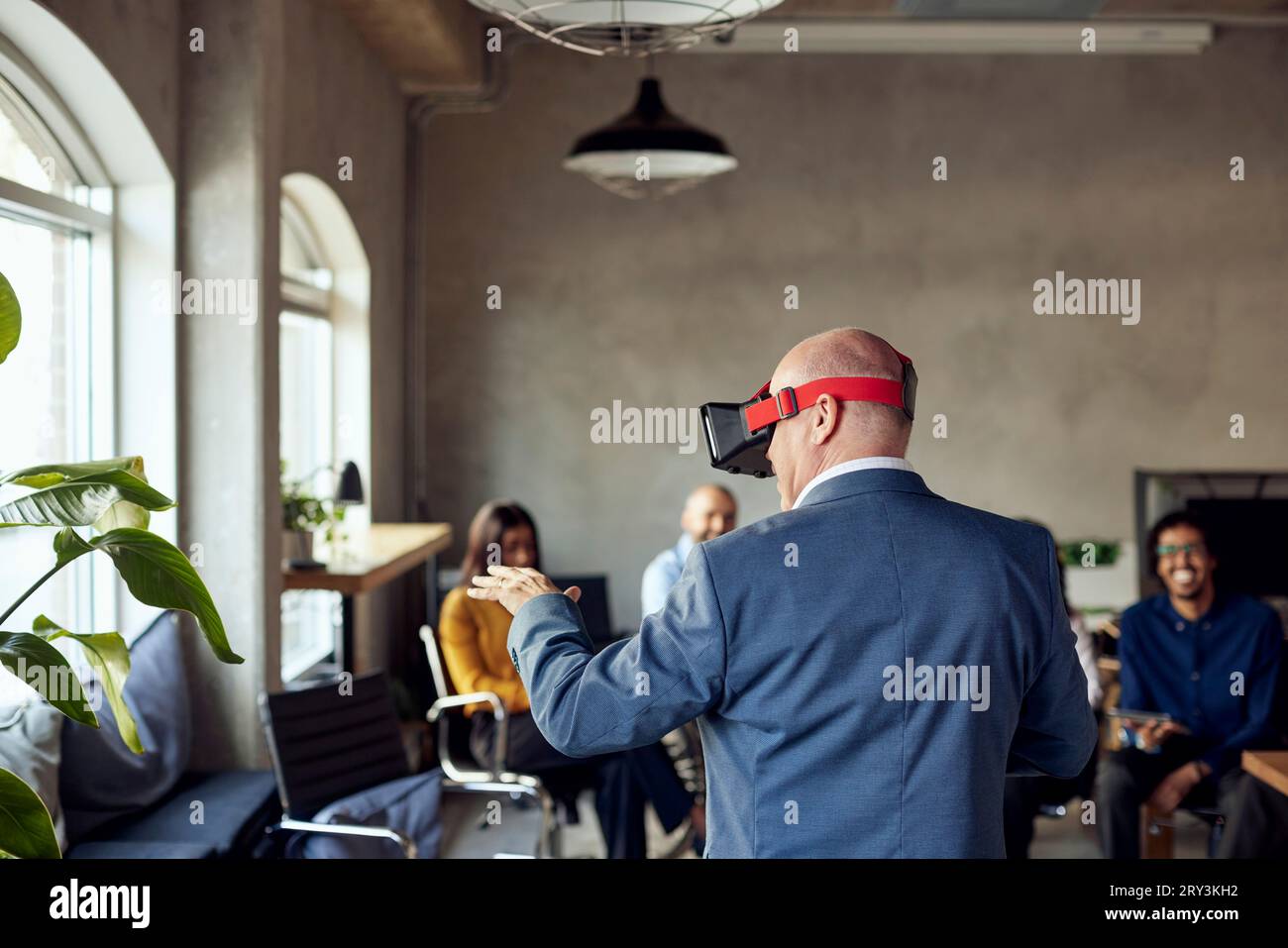 Rear view of mature businessman wearing VR gesturing at creative office Stock Photo
