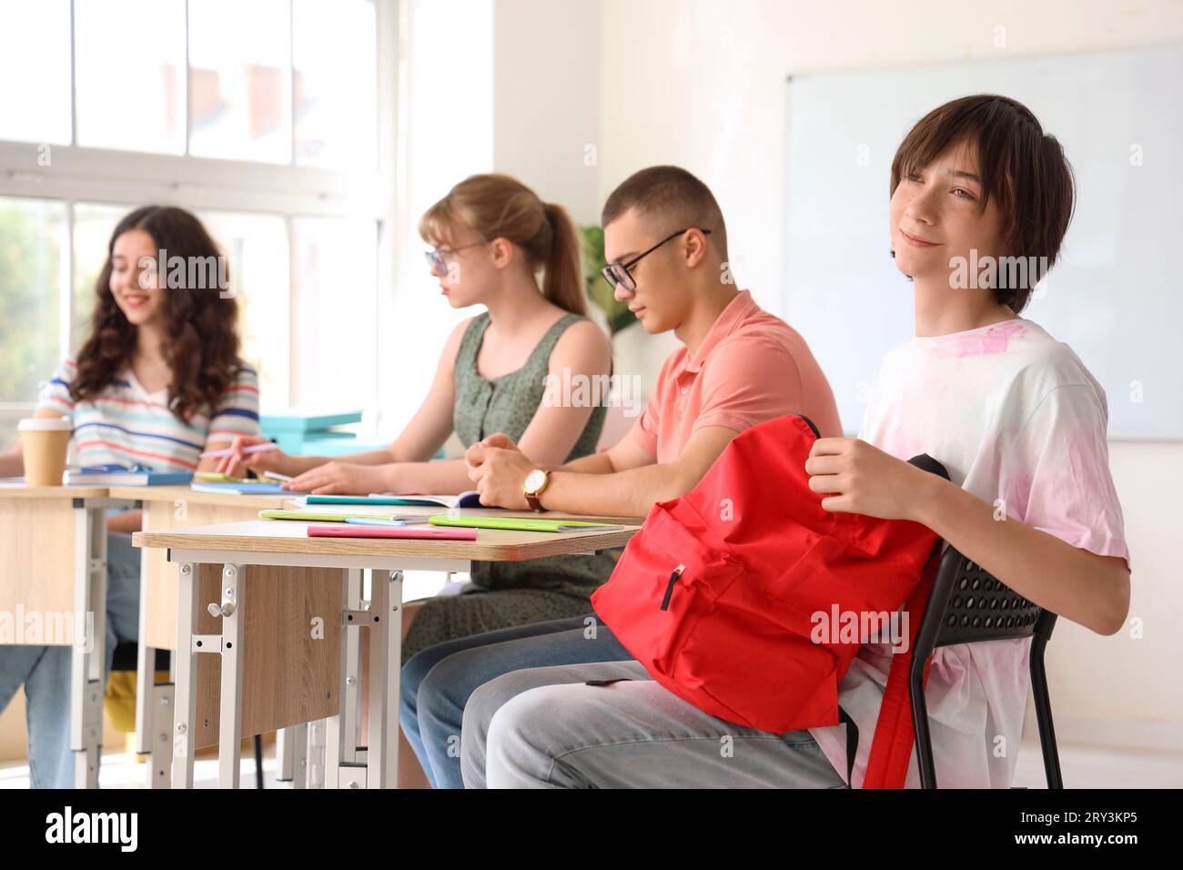 Male student with backpack and his classmates having lesson in classroom Stock Photo
