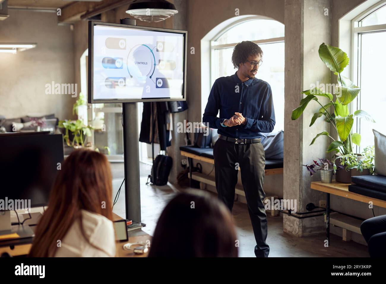 Businessman standing with hands clasped near television set during meeting Stock Photo