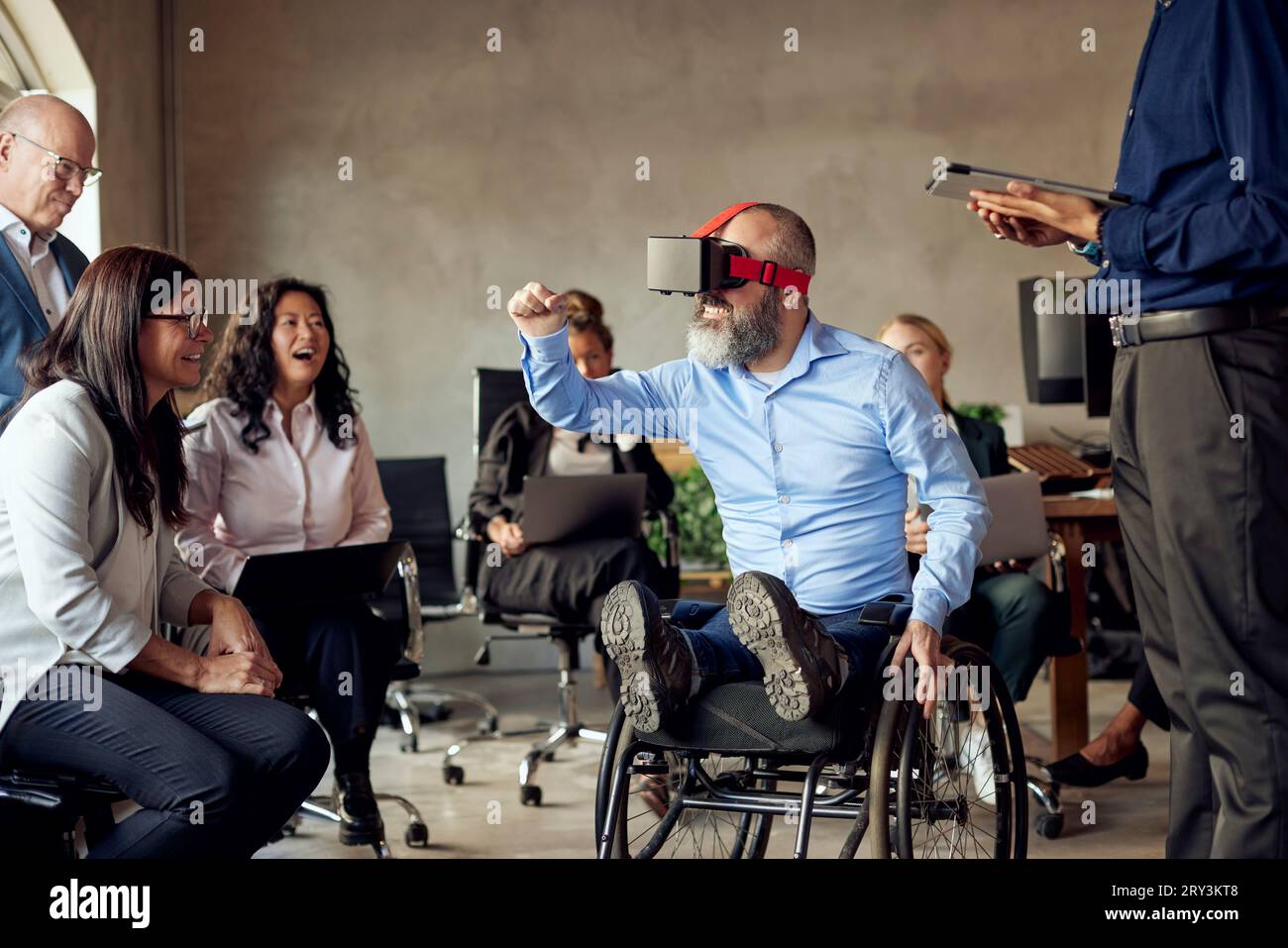 Male and female colleagues looking at businessman with disability watching VR at creative office Stock Photo