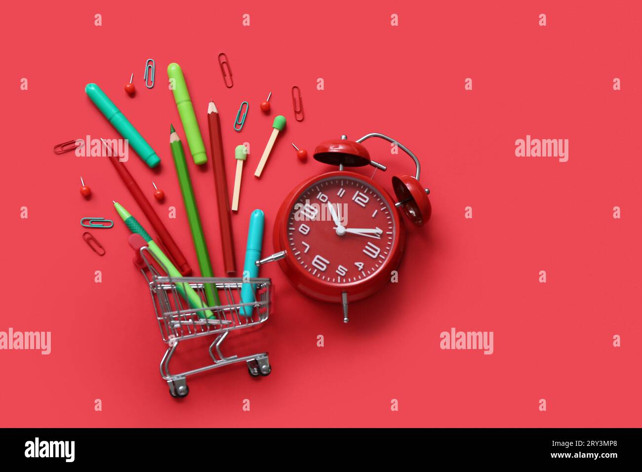 Alarm clock and shopping cart with different stationery on red background Stock Photo