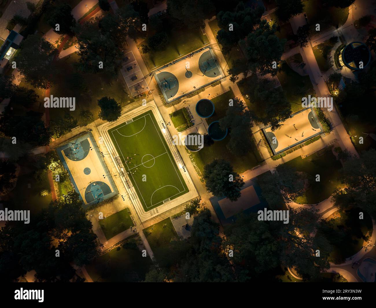 Sport courts at a park in aerial view. Evening photo about foutball, basketball courts and ping pong tables. Illuminated recreation park. Stock Photo