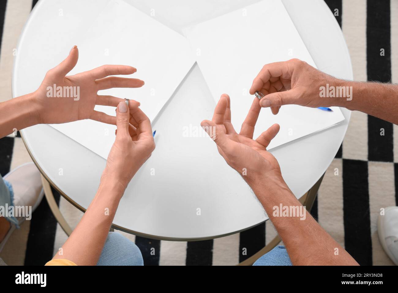 Divorced mature couple taking wedding rings off fingers in office, top