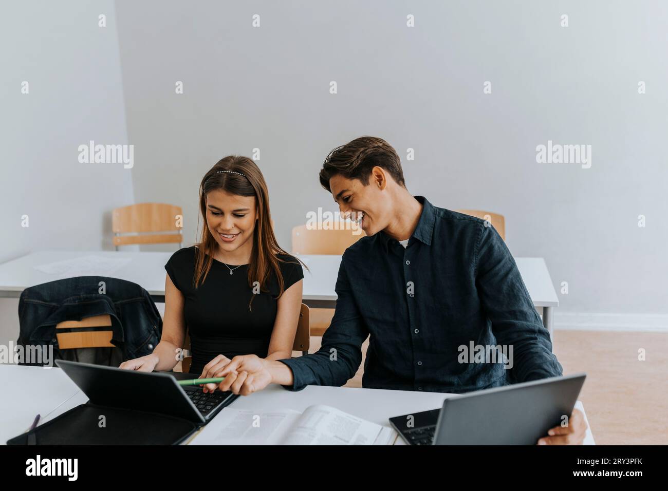 Smiling teenage boy and girl sharing laptop while studying together at ...