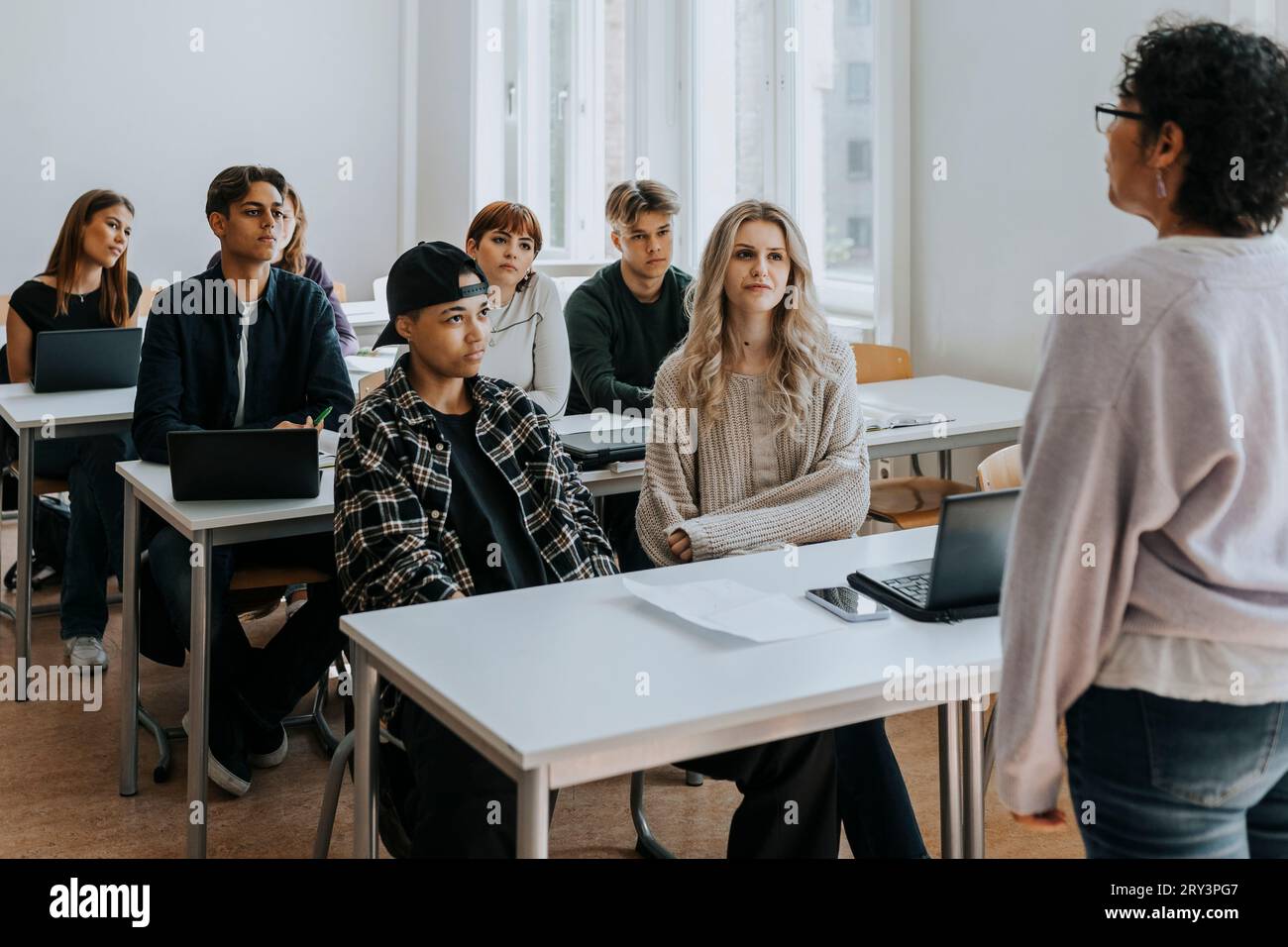 Multiracial students listening to teacher in classroom Stock Photo - Alamy