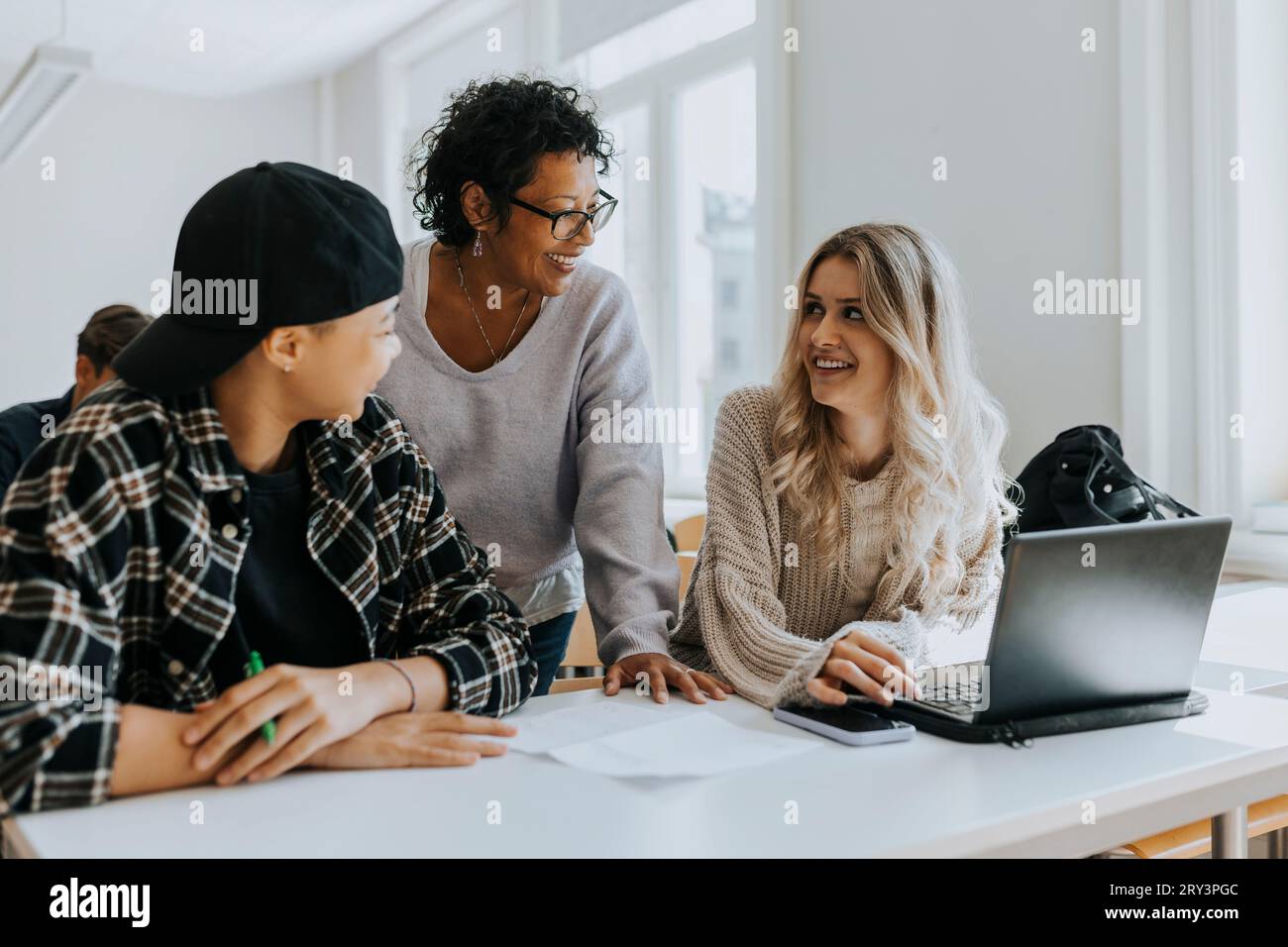 Happy teacher talking with young students at desk in classroom Stock Photo