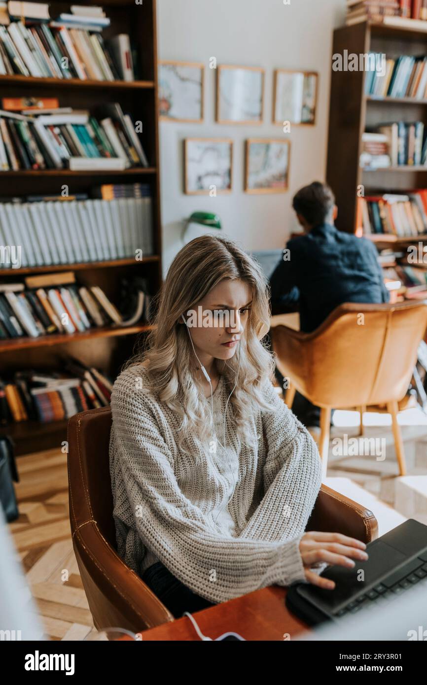 Blond young woman using laptop while sitting in library Stock Photo