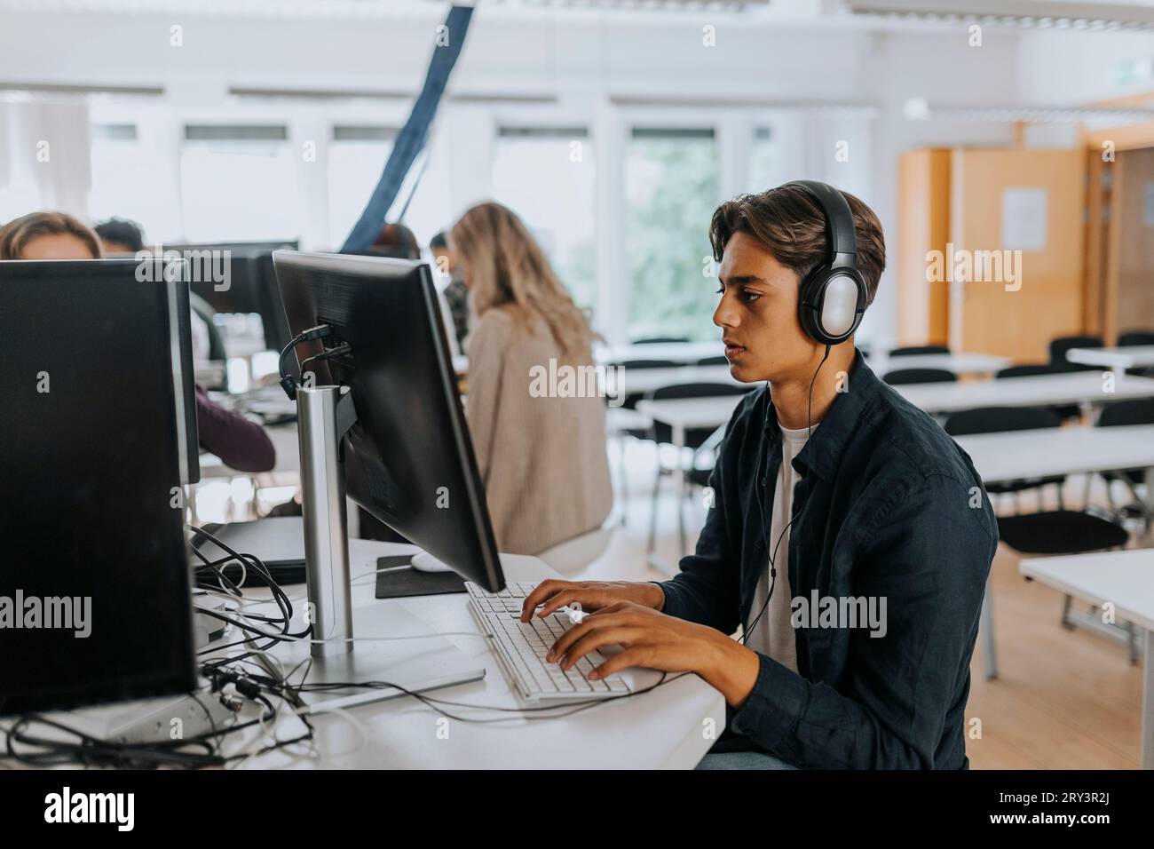 Teenage boy listening through headphones while using computer in school