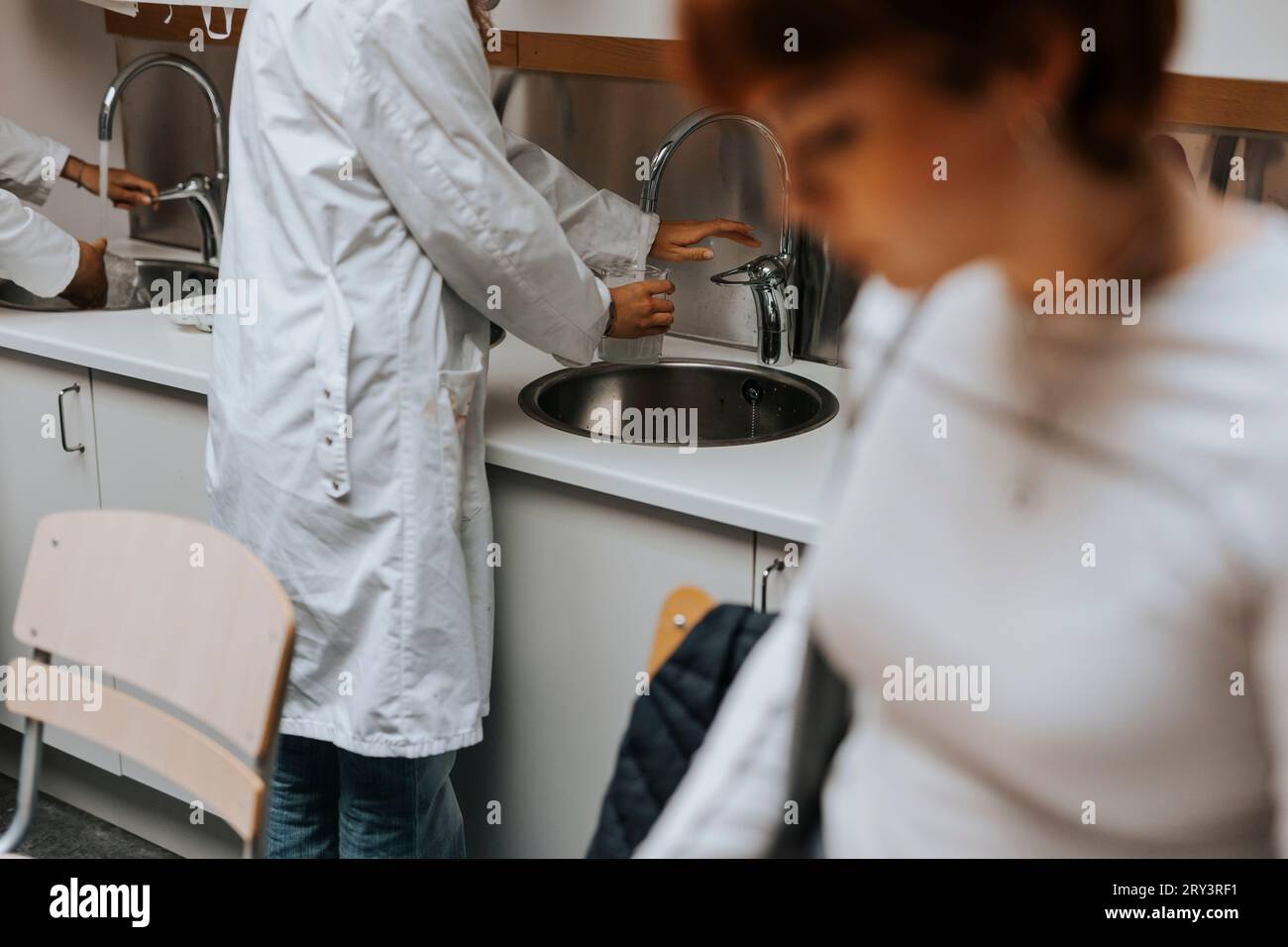 Midsection of female young student washing beaker in sink at science lab Stock Photo