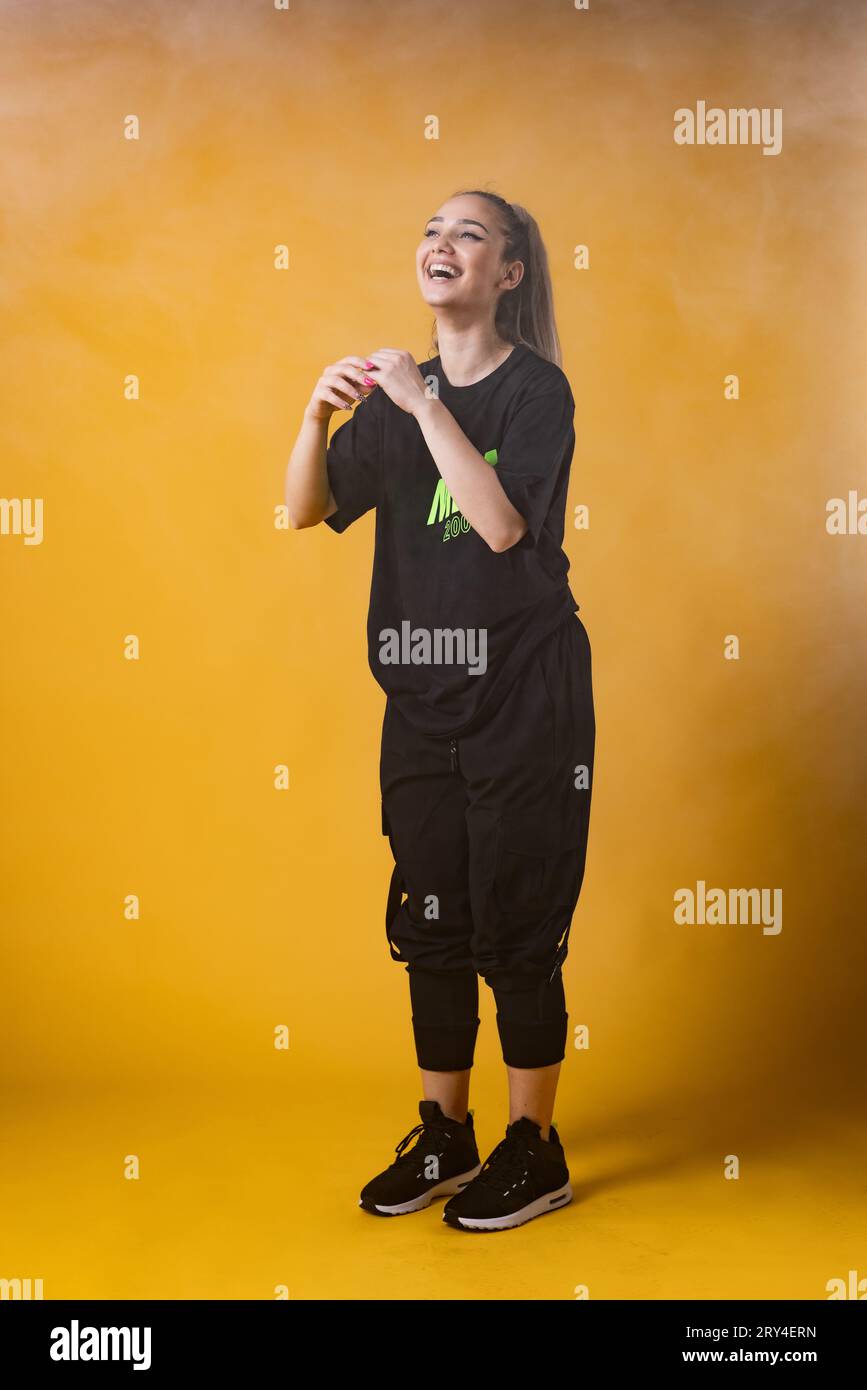 Beautiful girl in black outfit smiling. Happy dance instructor against dark yellow or orange background. Stock Photo