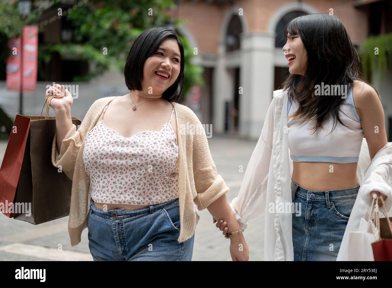 A cheerful and pretty Asian plus-size woman enjoys spending her weekend with her friend in the city and going on a shopping spree together. Stock Photo