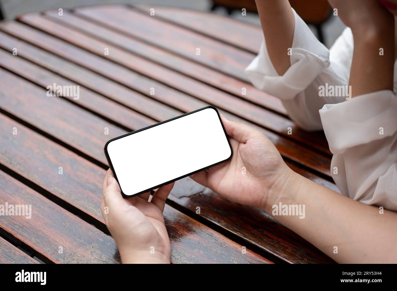 Close-up image of a woman holding a white-screen smartphone mockup in a horizontal position while sitting at a table with her friend. watching video, Stock Photo