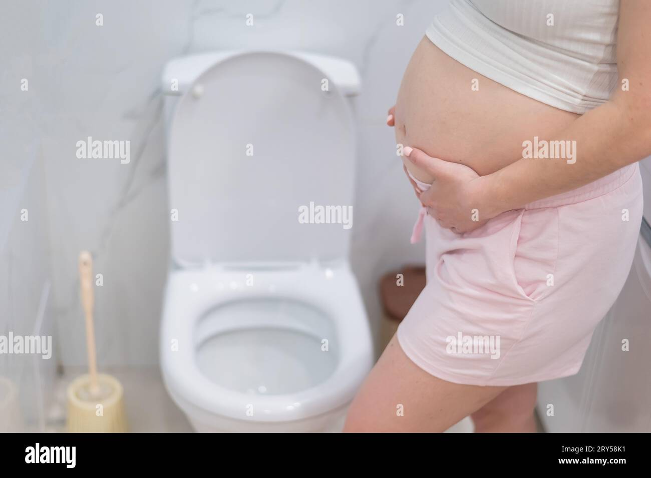 Pregnant woman holding her belly in the toilet. incontinence during ...