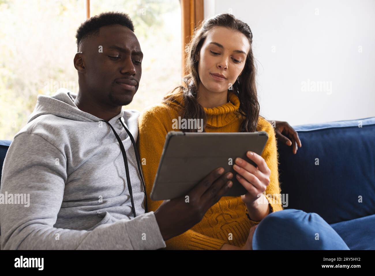 Diverse couple sitting on sofa using tablet at home Stock Photo
