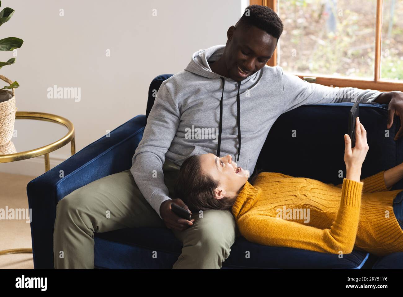 Happy diverse couple sitting on sofa using smartphones at home Stock Photo