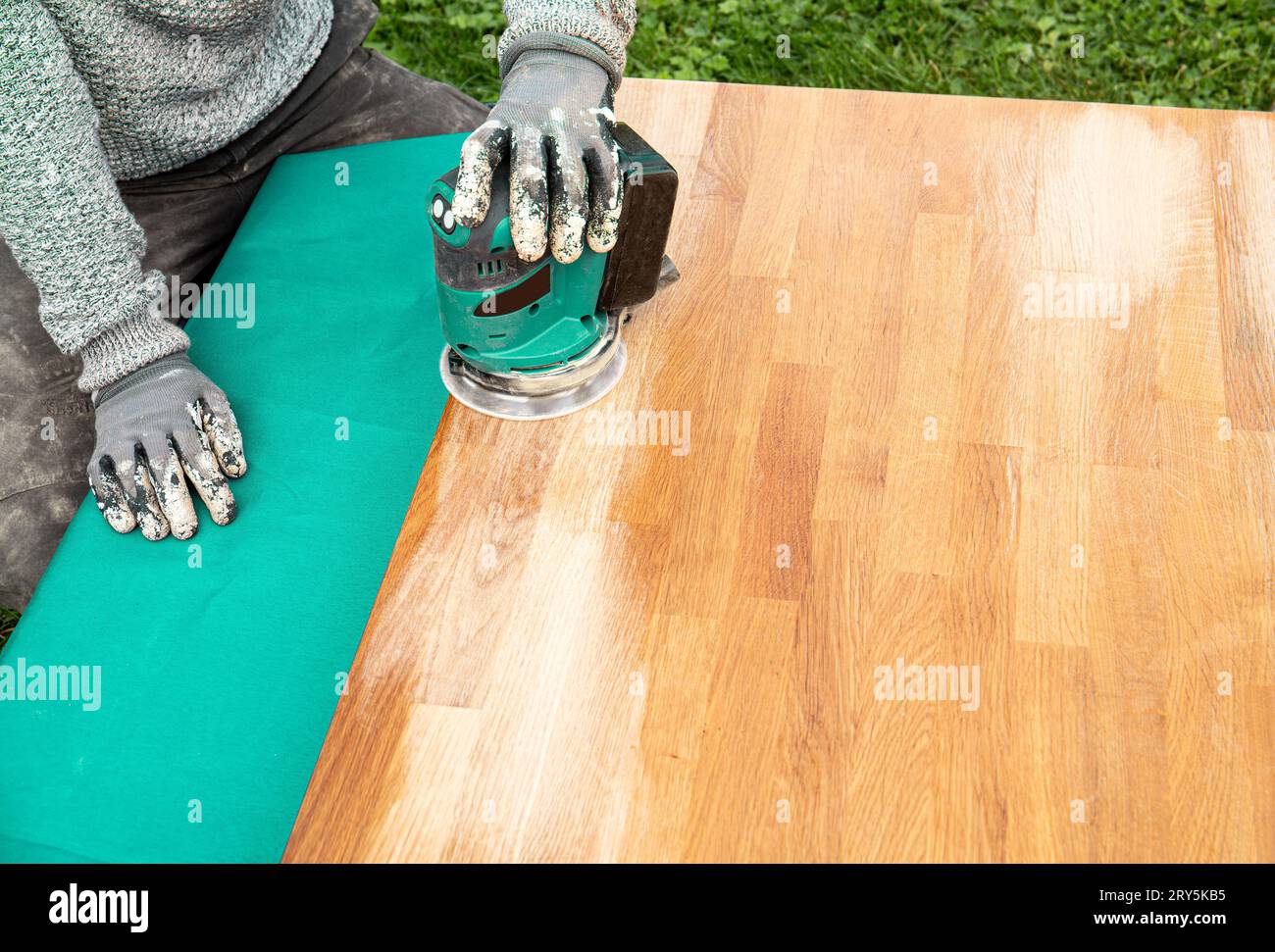 Close up view of person working with sander tool, sanding off stains on old damaged butcher block on oiled wood table. Renovation concept. Stock Photo