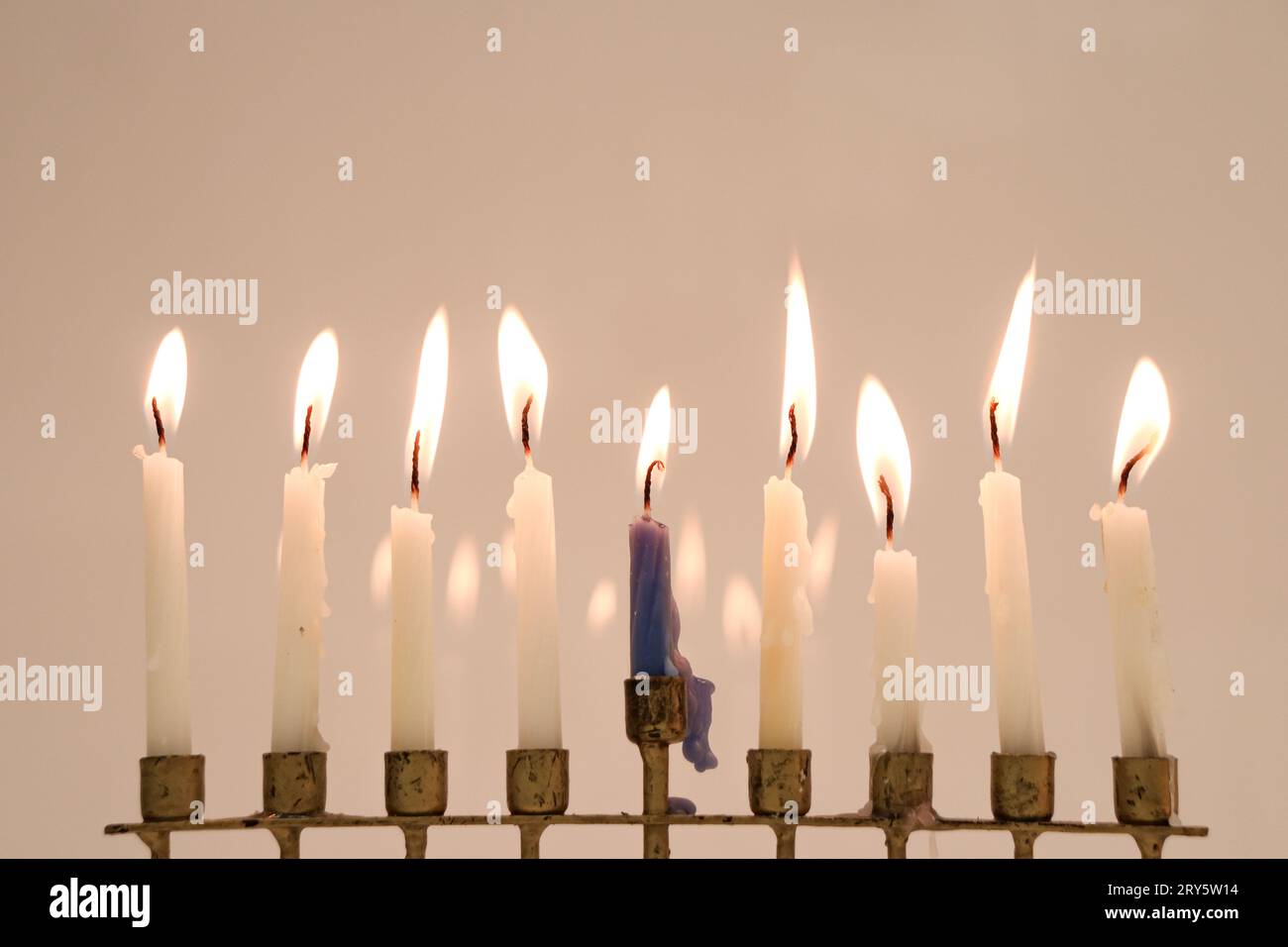 A full menorah on the last night of Hanukkah. Eight white candles and the center is blue. All candles are lit and reflecting in the back Stock Photo