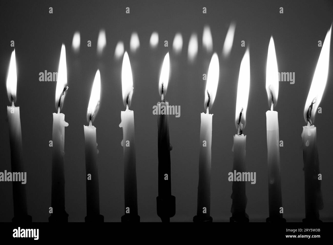 Black and white full menorah on the last night of Hanukkah. All nine candles are lit in a dark room and reflecting in the background. Holiday concept Stock Photo
