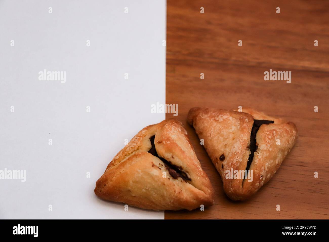 Hamantash (Ozen Haman), an Ashkenazi Jewish triangular filled-pocket pastry traditionally eaten during Purim holiday isolated on half white and half w Stock Photo