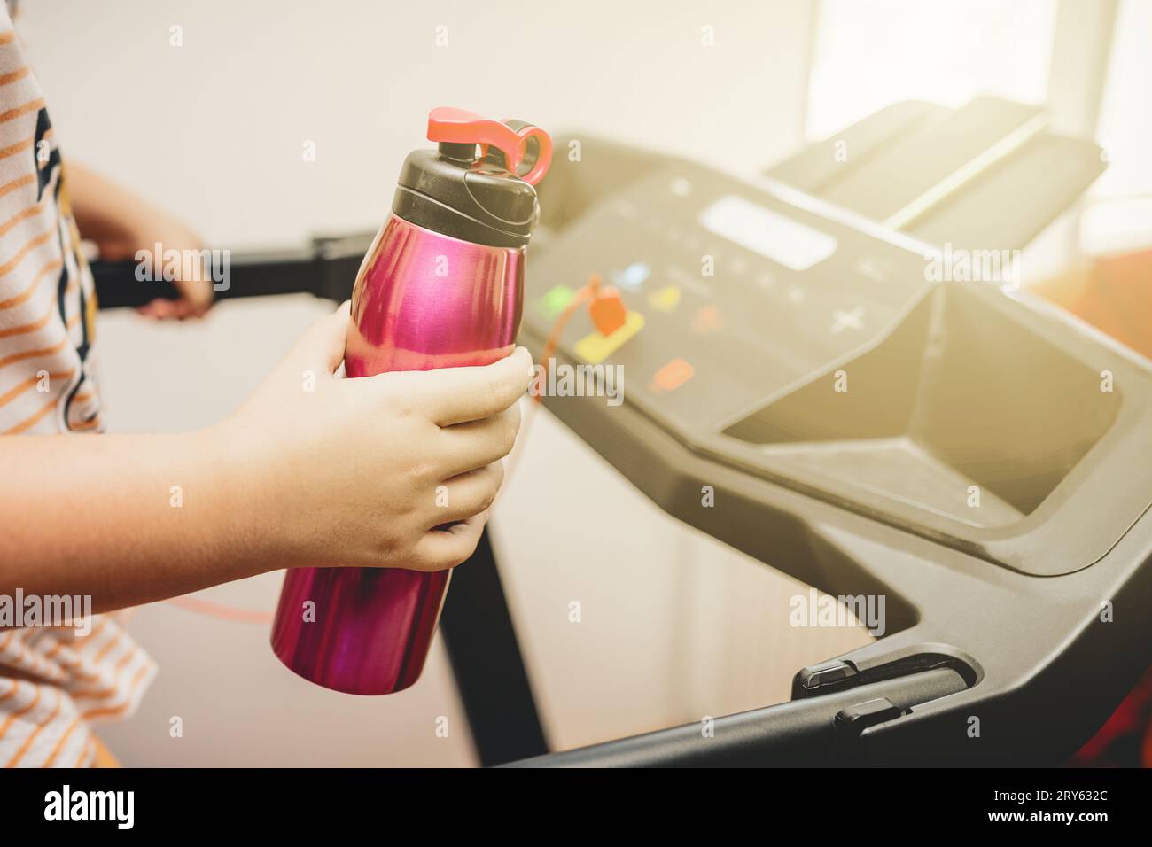 Young girl running on the treadmill with a sports water bottle in hand