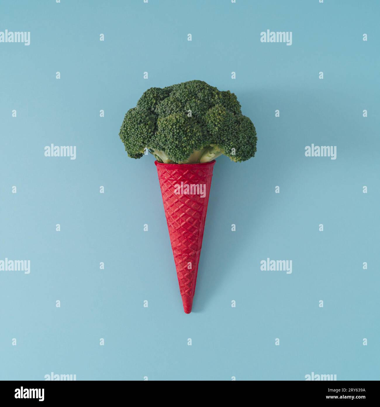 Pink waffle ice cream cone with broccoli on light blue background. Minimal food concept. Summer