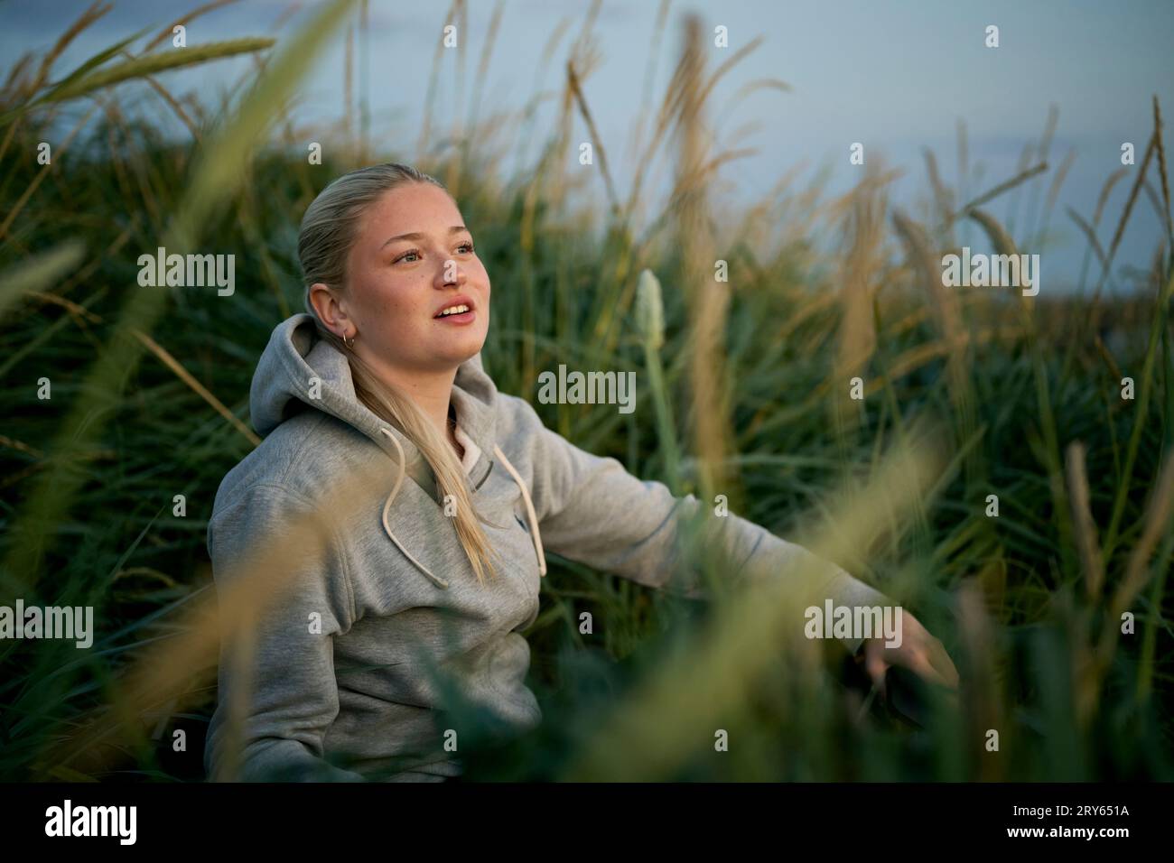 Young blonde woman sitting in countryside field in summer evening Stock Photo