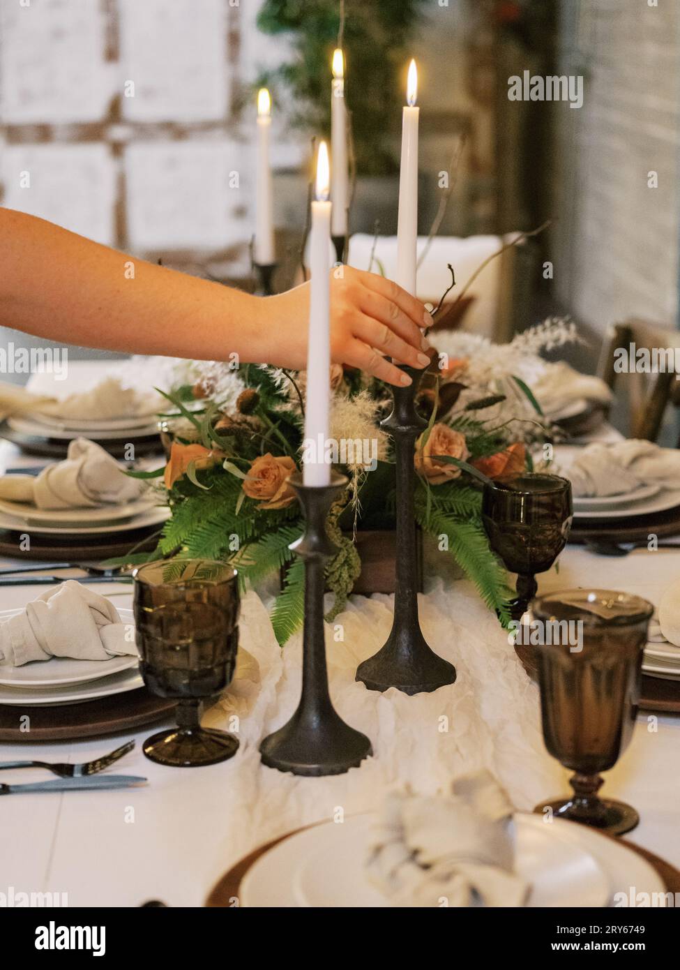Woman adjusts taper candle in autumn table setting, vintage glas Stock Photo