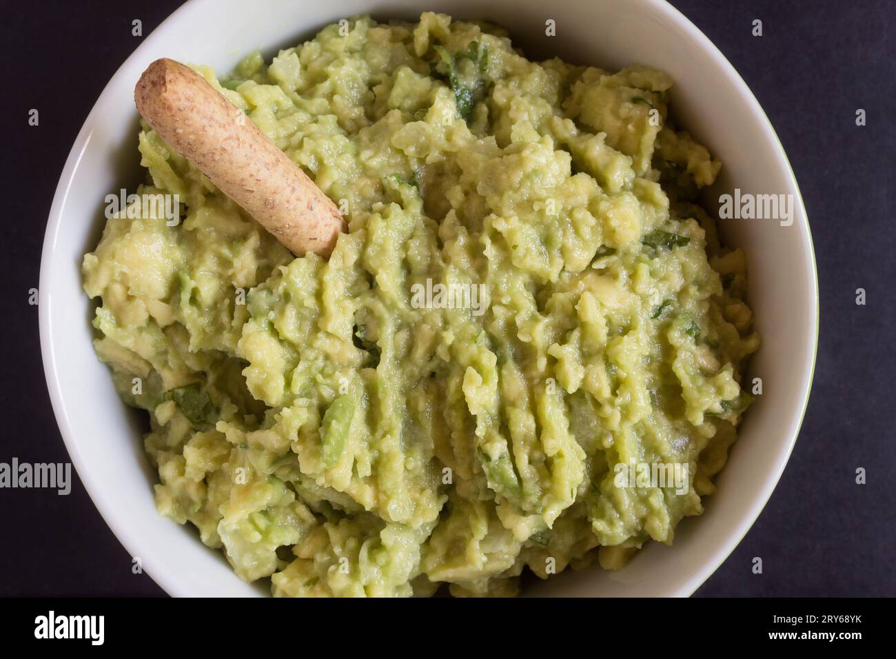 A macro shot of a delicious homemade guacamole dip in a round bowl, garnished with a crunchy whole grain breadstick. Traditional food Stock Photo