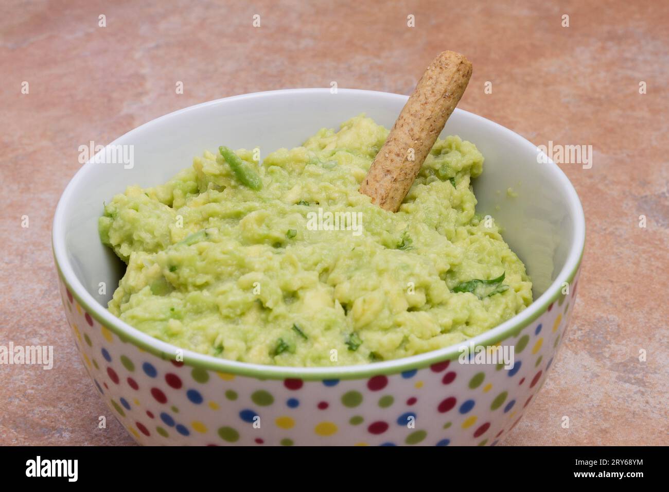 Close-Up View  of Homemade Guacamole, Nestled in a Decorative Bowl Adorned with Vibrant Color Dots Set Against a Rustic Kitchen Countertop with Stone- Stock Photo