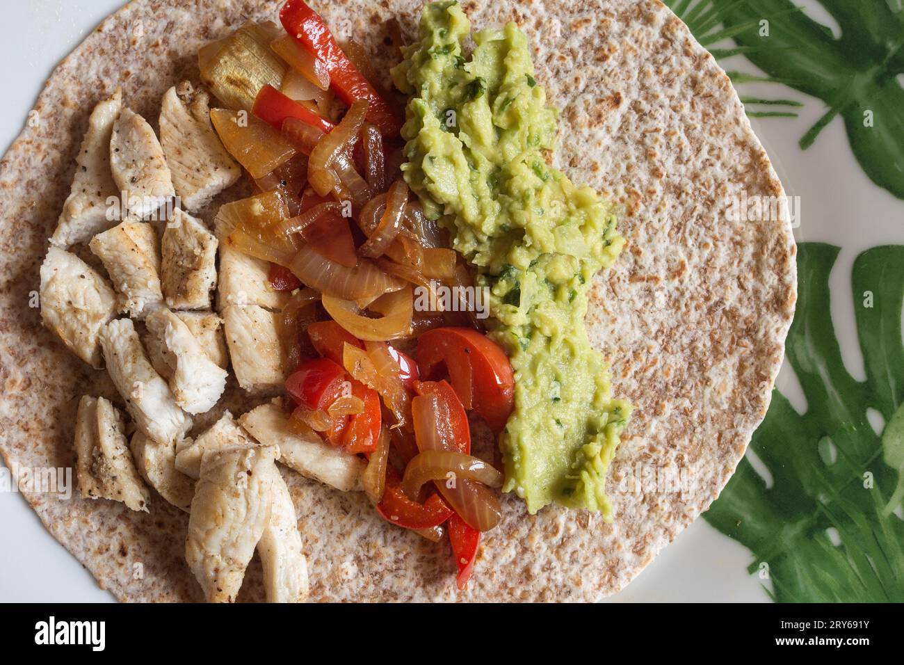 Overhead view of an Open Whole Wheat Chicken Fajita Tortilla Served on a plate with succulent seasoned chicken, vibrant veggies, and guacamole. Stock Photo