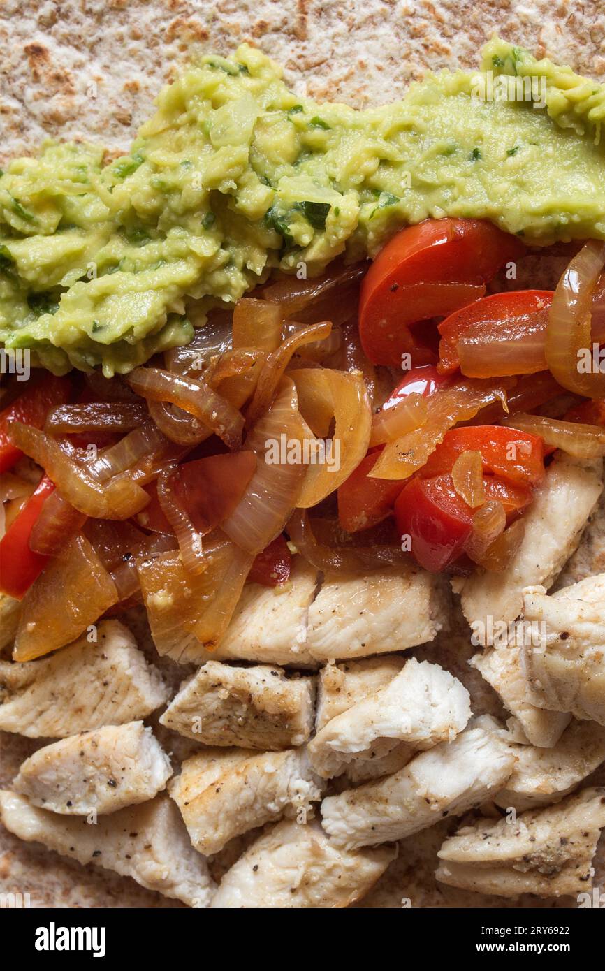 A close-up overhead view of homemade Mexican fajita ingredients featuring guacamole, cumin-seasoned chicken, onion, and semi-raw red pepper, artfully Stock Photo