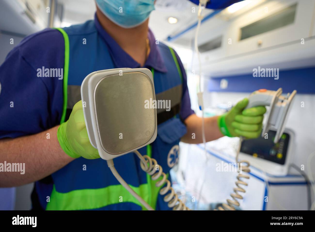 Ambulance doctor with defibrillator electrodes in his hands, a paramedic is in an ambulance