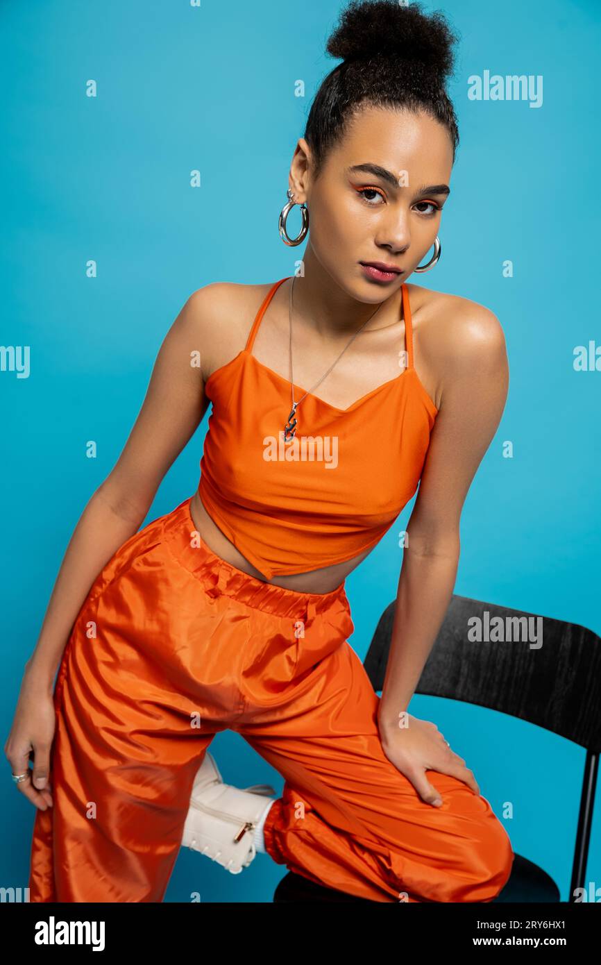 beautiful fashion model in orange outfit posing on tall chair looking