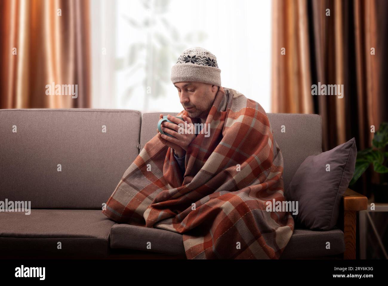 Middle age male model in hat and plaid hold coffee cup sitting on the sofa Stock Photo