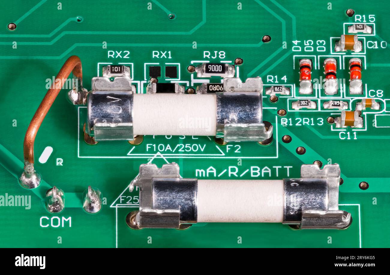 Close-up of ceramic tubes of electrical fuses in metal holder on circuit board. Low ohm wire resistor for current measuring, capacitors or red diodes. Stock Photo