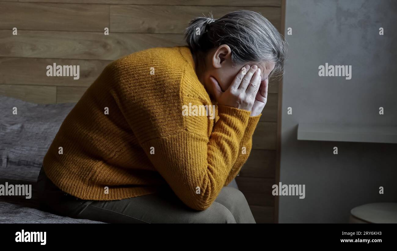 Mature woman with severe headache sitting on bed in bedroom Stock Photo ...