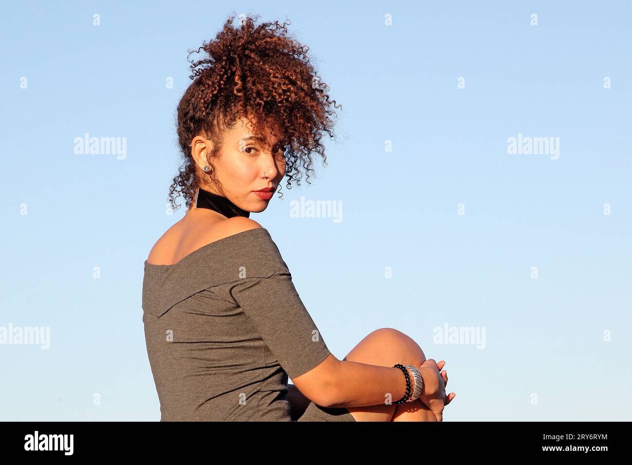 Curly hair woman in brown dress posing with blue sky in background Stock Photo