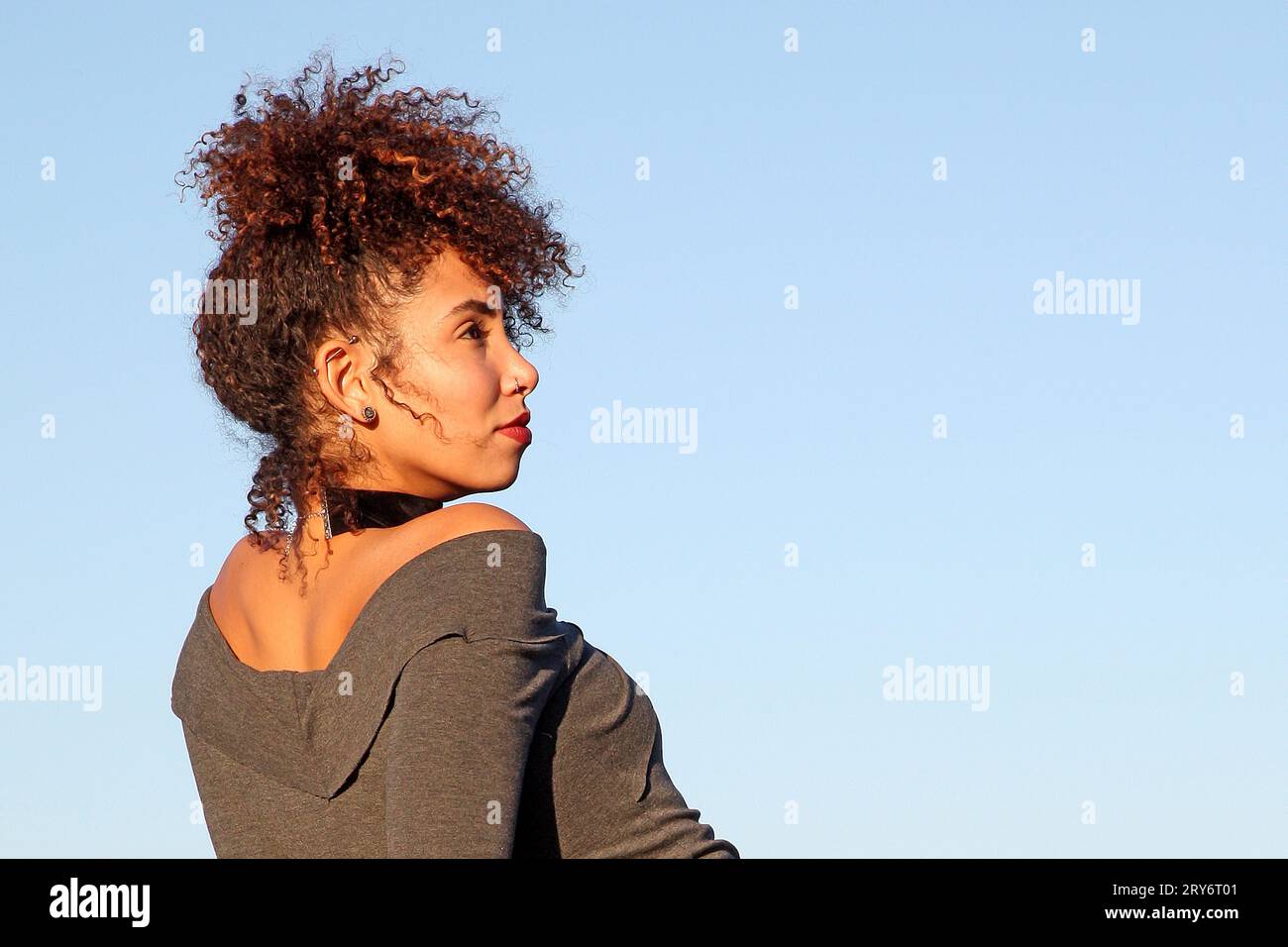 Curly hair woman in brown dress posing with blue sky in background Stock Photo