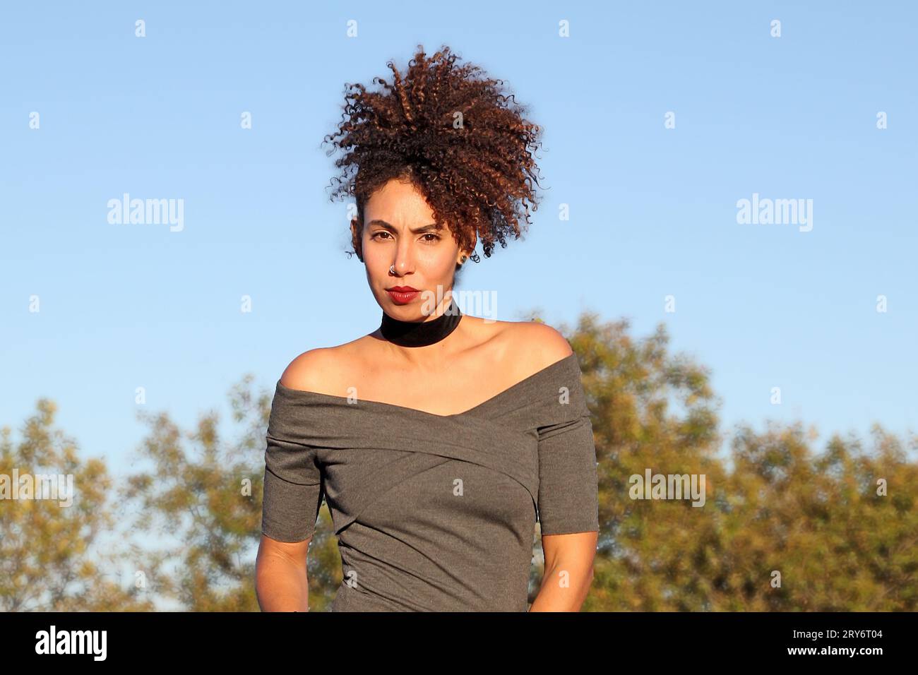 Curly hair woman in brown dress posing with blue sky in background Stock Photo
