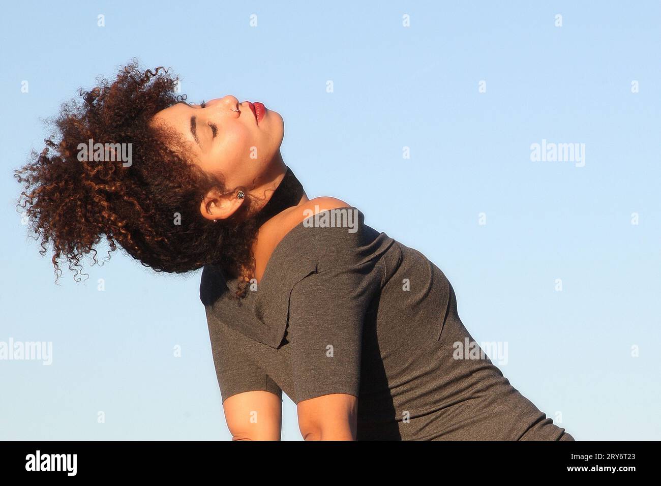 Curly hair woman in brown dress posing with blue sky in background Stock Photo