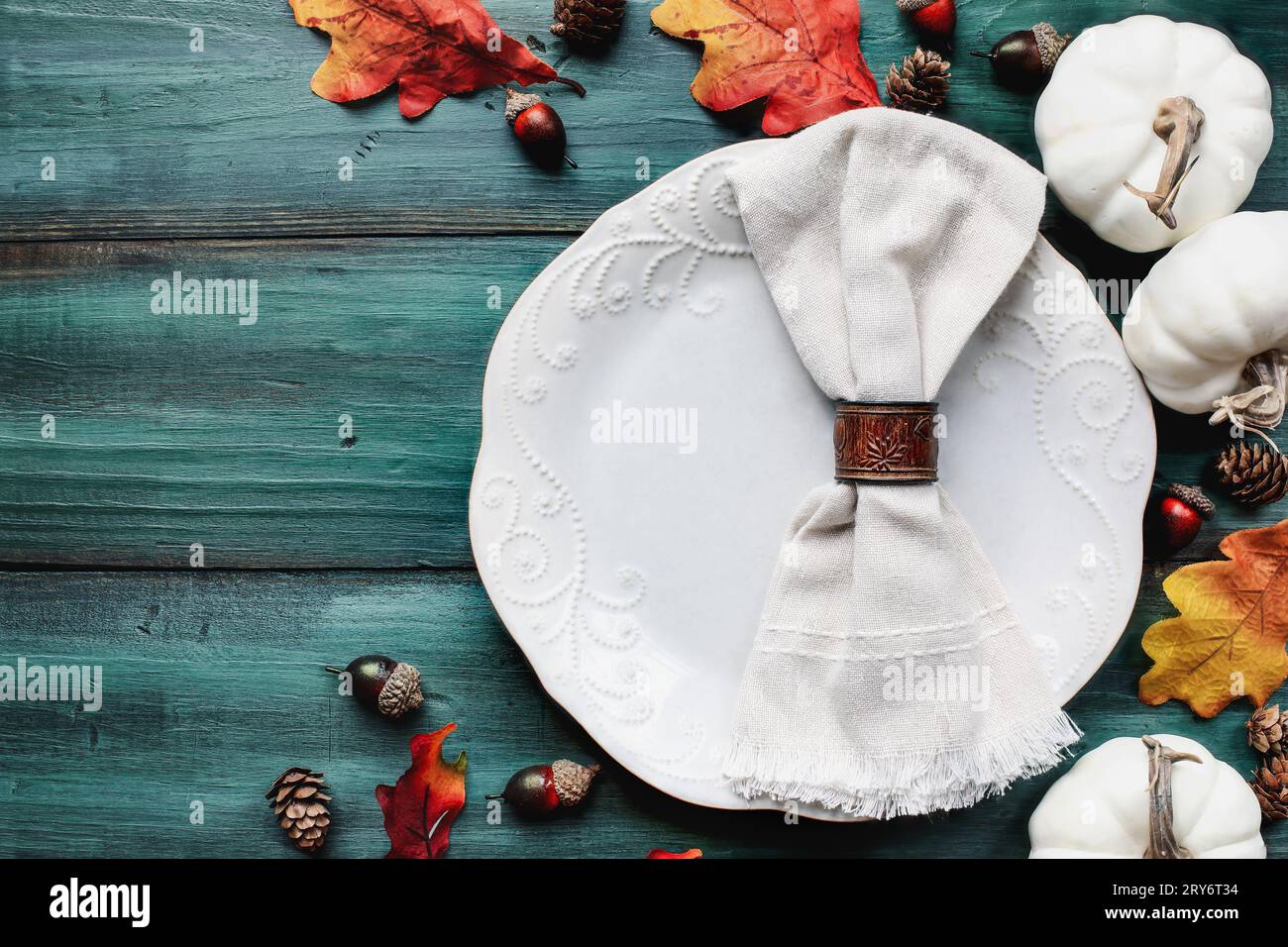 Flat lay of a white plate with napkin. Place setting over a rustic wood table with colorful autumn leaves. Table top view. Stock Photo