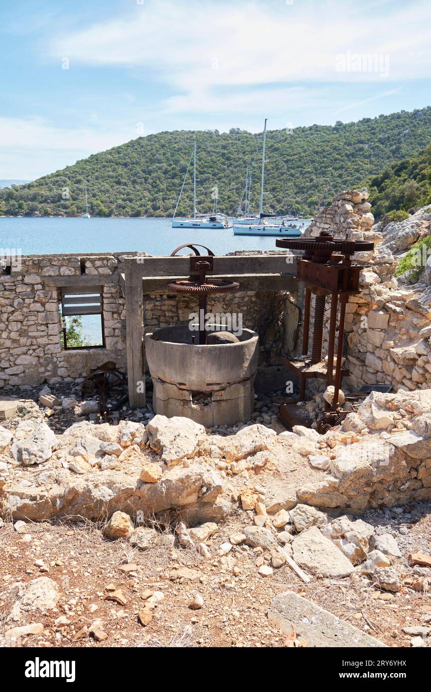 Olive Press in ruins of Port Leone, with sailing boats at anchor in background on Kalamos Island, Ionian, Greece. Stock Photo
