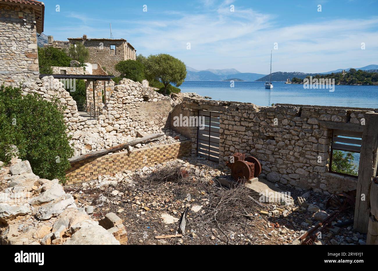 Olive Press in ruins of Port Leone, with sailing boat at anchor in background on Kalamos Island, Ionian, Greece. Stock Photo