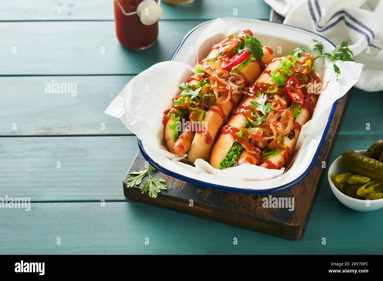 Delicious grilled hotdog with pickled  cucumbers, chili peppers, caramelized onions, ketchup, mustard in craft paper on blue old wooden background. Ho Stock Photo