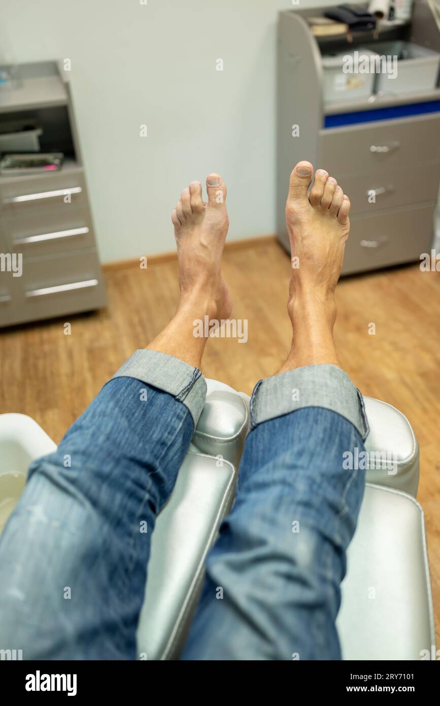 concept of male pedicure, foot pedicure, cosmetologist makes classic pedicure for an elderly