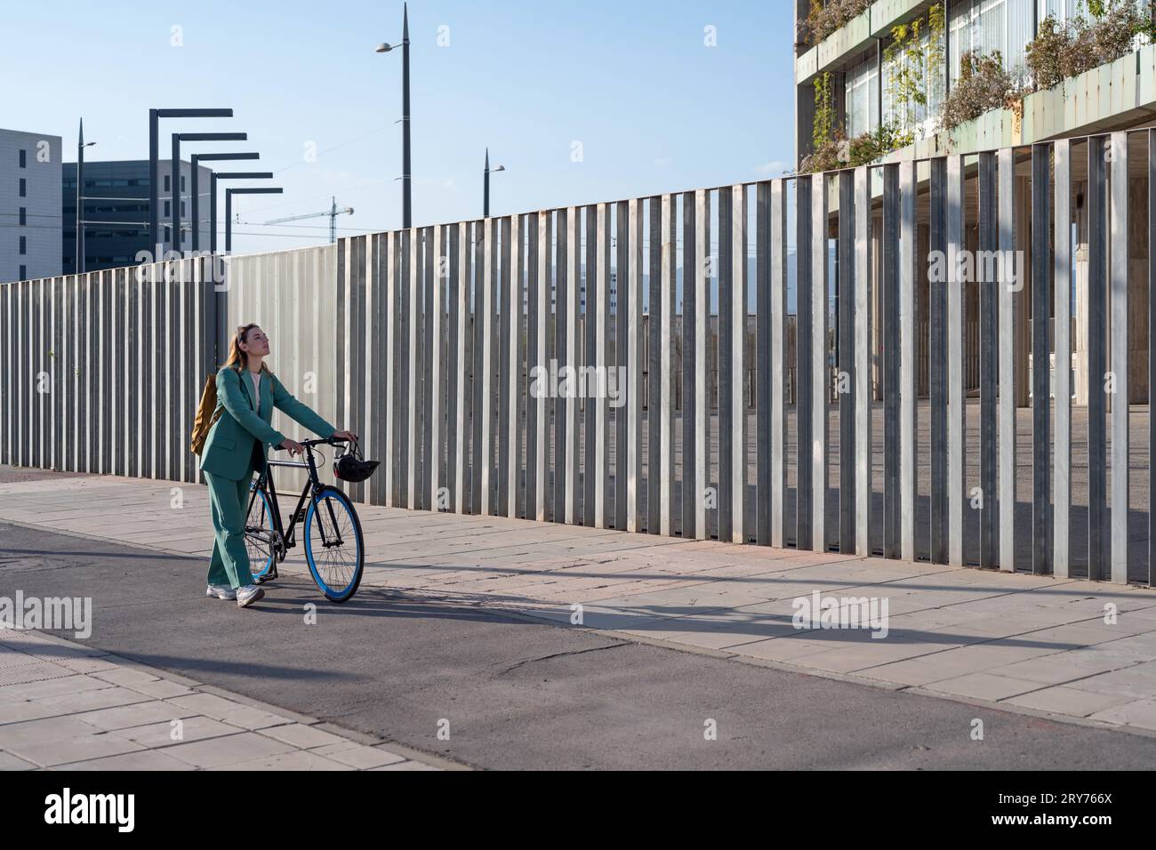 Stylish business woman in green suit walking with bicycle at the financial district with modern building on the background Stock Photo