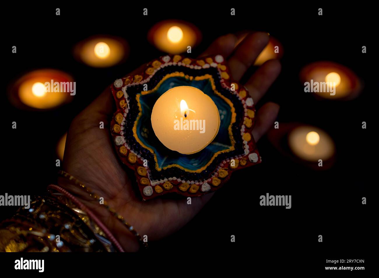 Happy Diwali - Woman hands with henna holding lit candle isolated on dark background. Clay Diya lamps lit during Deepavali, Hindu festival of lights. Stock Photo