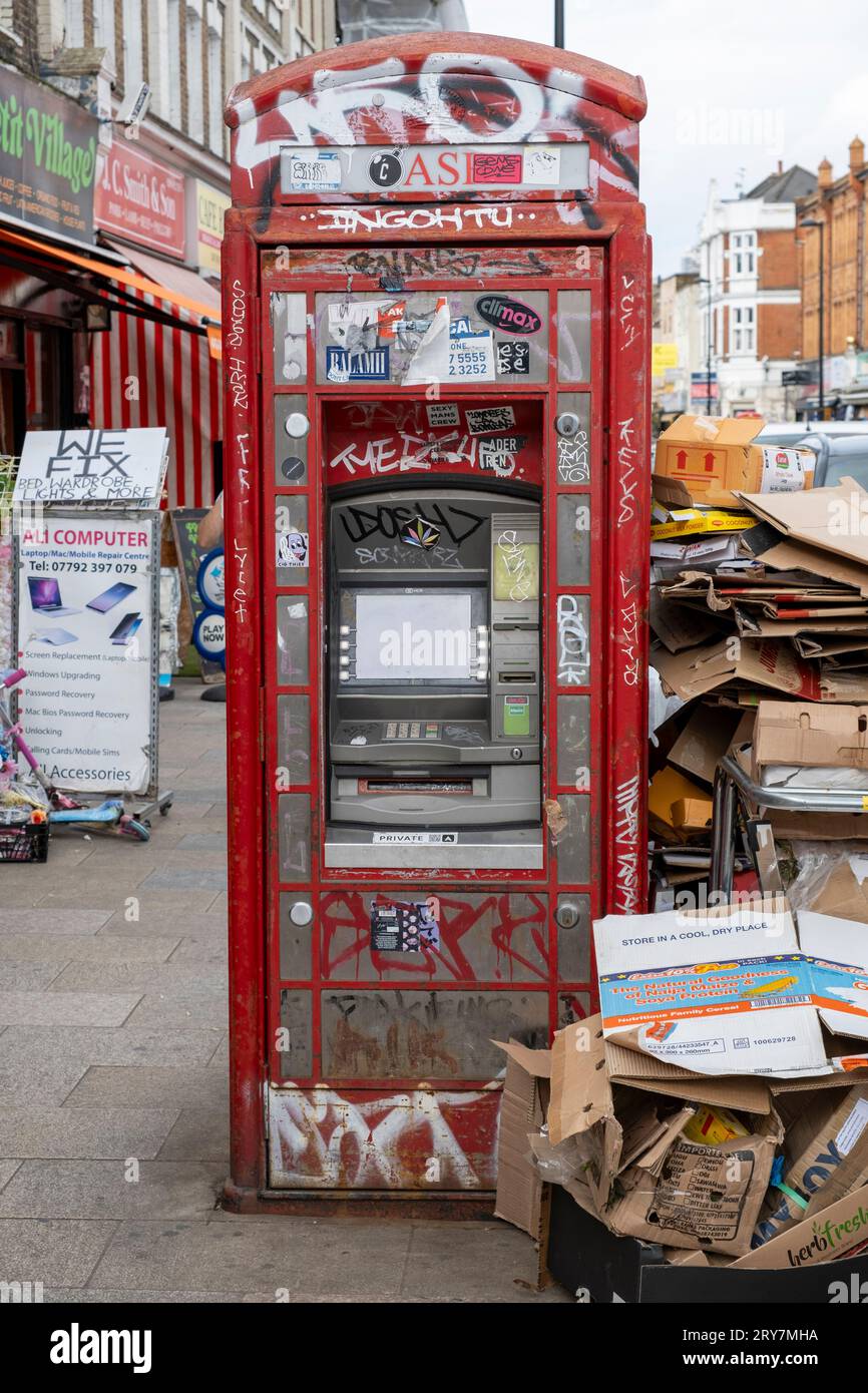 Iconic red telephone phone box converted into a cash dispenser machine surrounded by discarded cardboard boxes on Deptford High Street, London Stock Photo